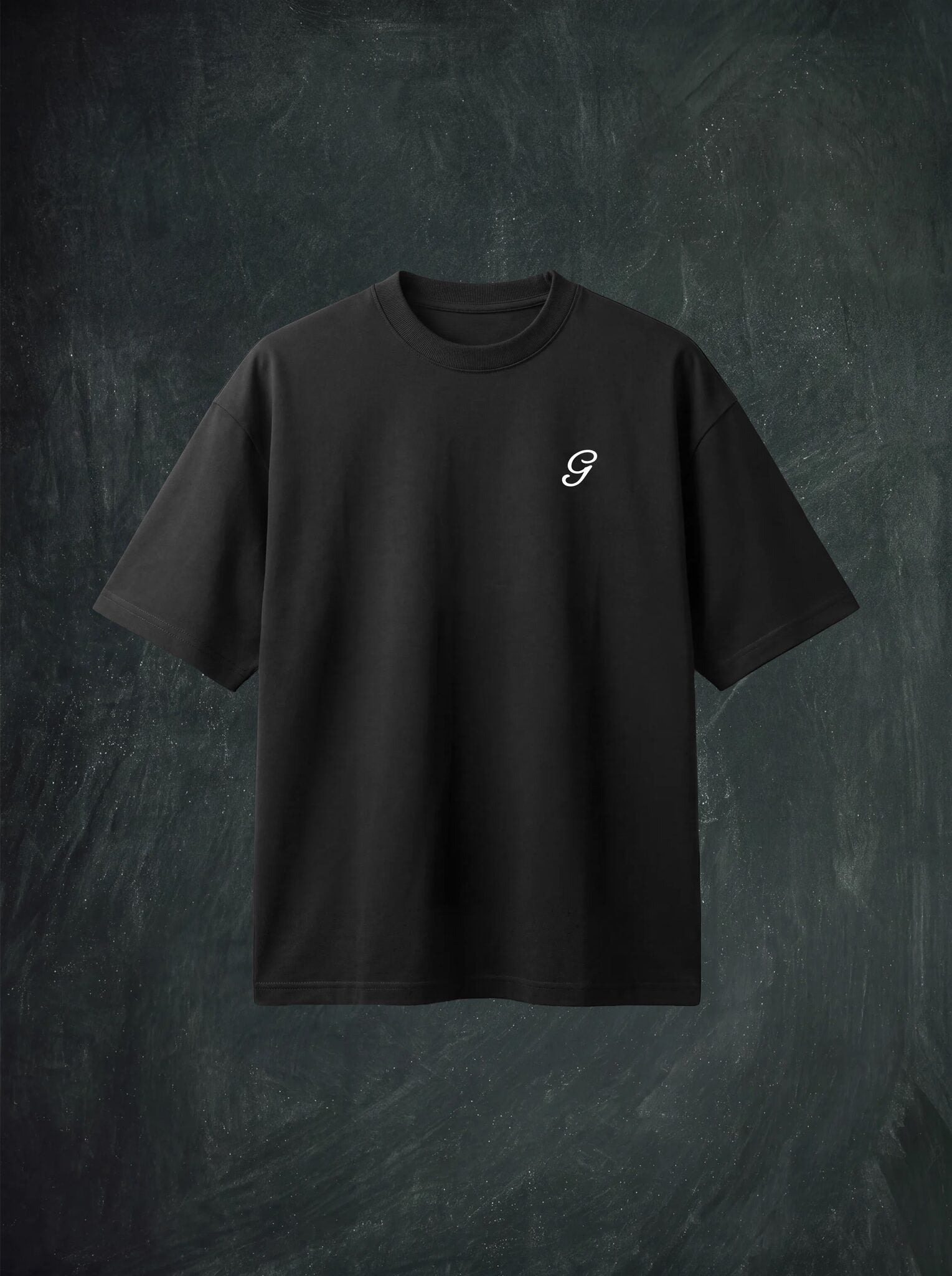 A black short-sleeve crewneck t-shirt with a small cream stylized 'G' logo on the left chest, displayed against a dark textured chalkboard background.