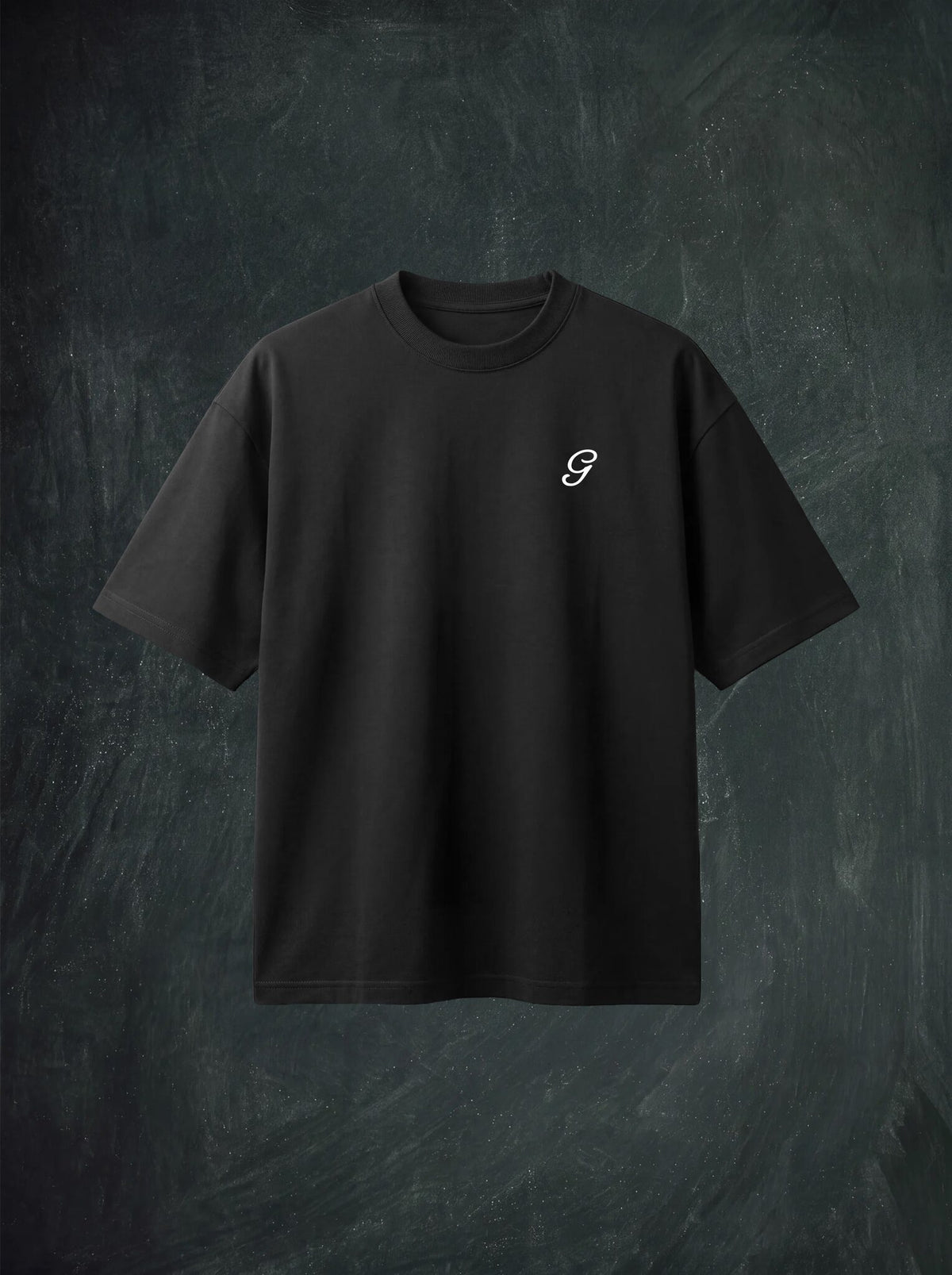 A black short-sleeve crewneck t-shirt with a small cream stylized 'G' logo on the left chest, displayed against a dark textured chalkboard background.