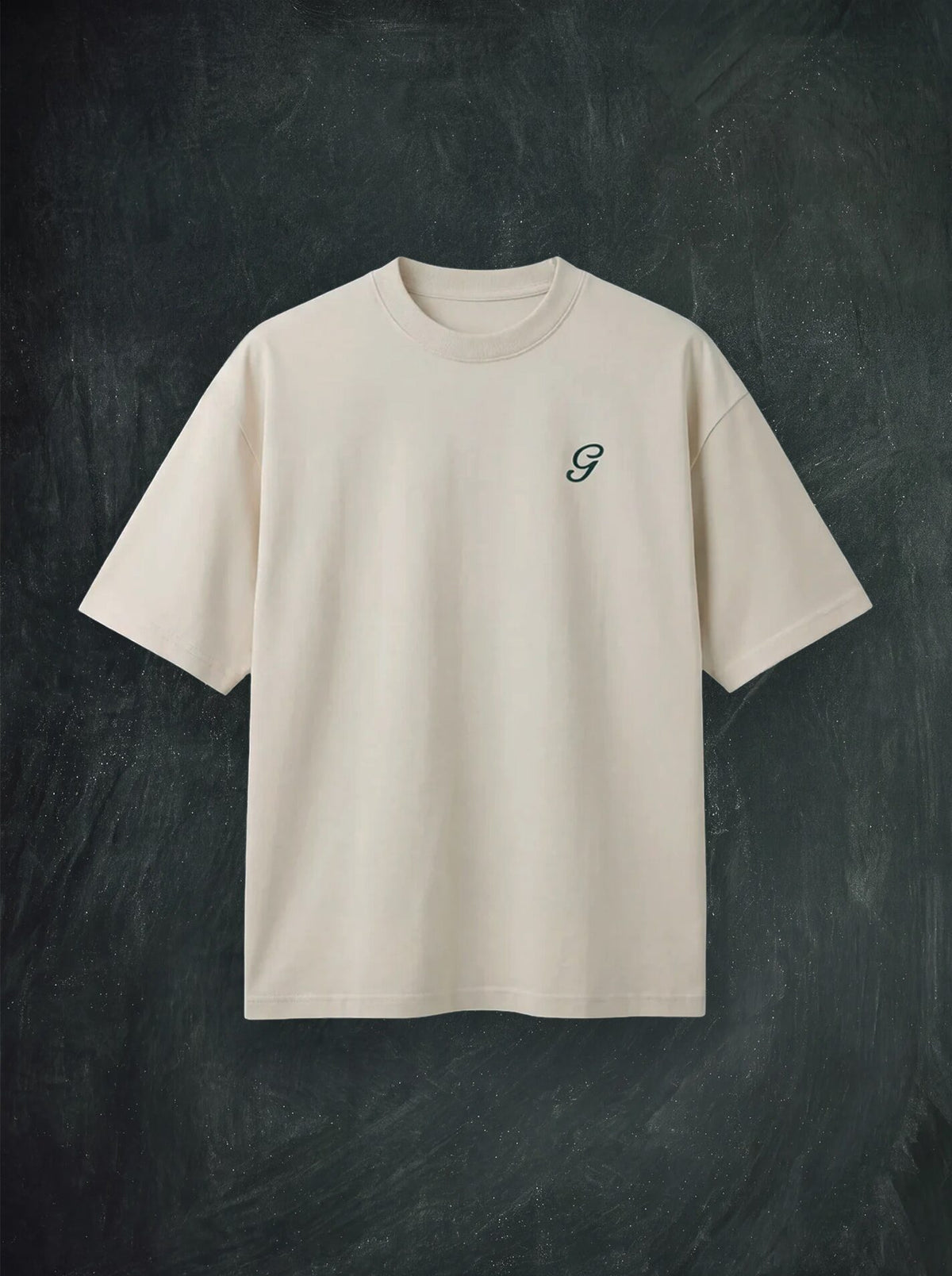 An off-white short-sleeve crewneck t-shirt with a small dark green embroidered script 'G' on the left chest, displayed flat against a dark textured chalkboard background.